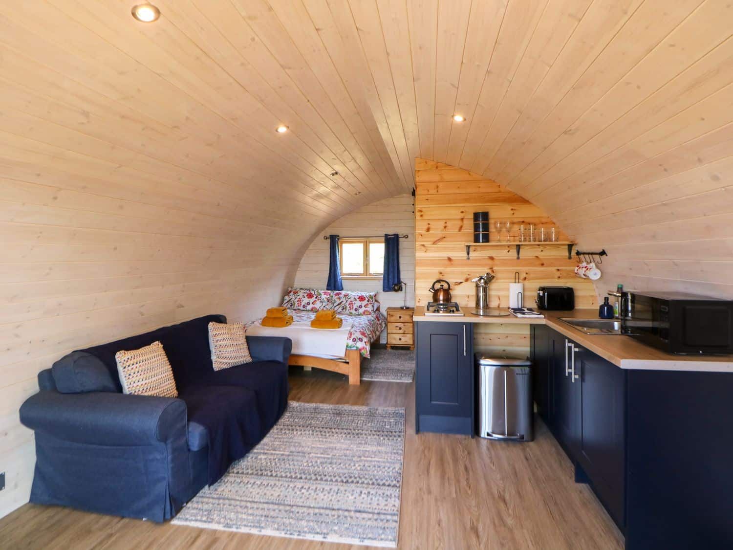 Curved timber interior with woodburning stove and cosy seating at Holbein pod