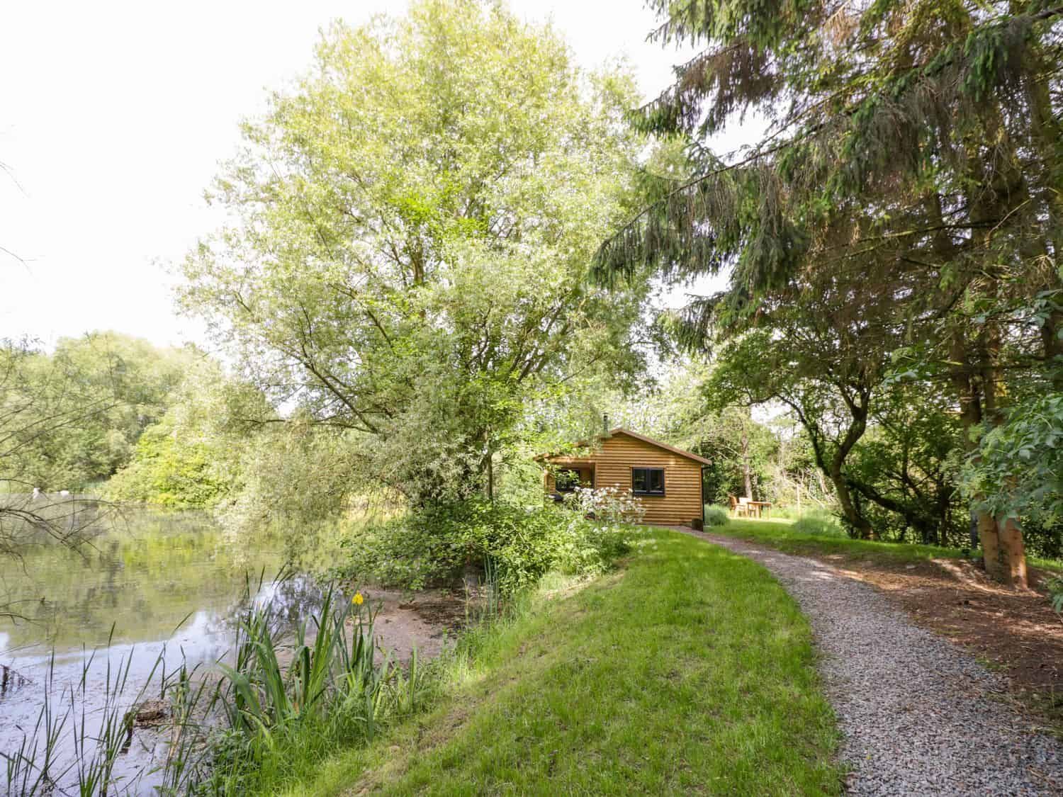 Willow wooden cabin near a pond with trees and gravel path