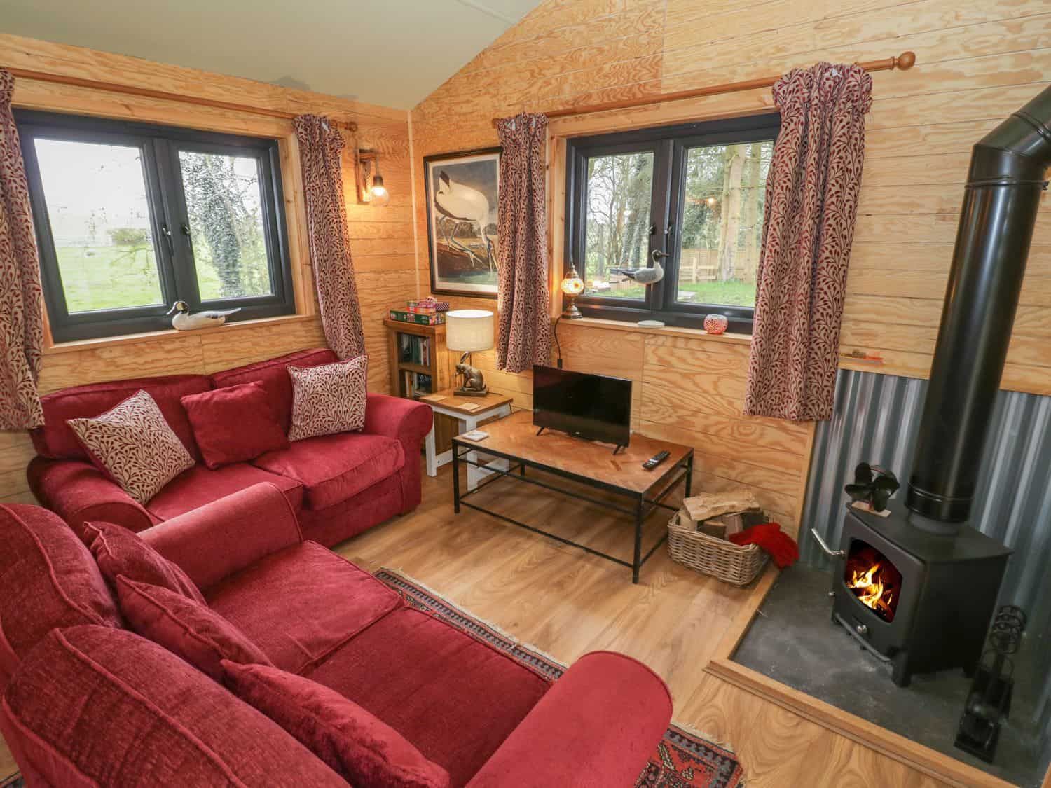 Sitting room with red sofas and wood burning stove at Willow cabin